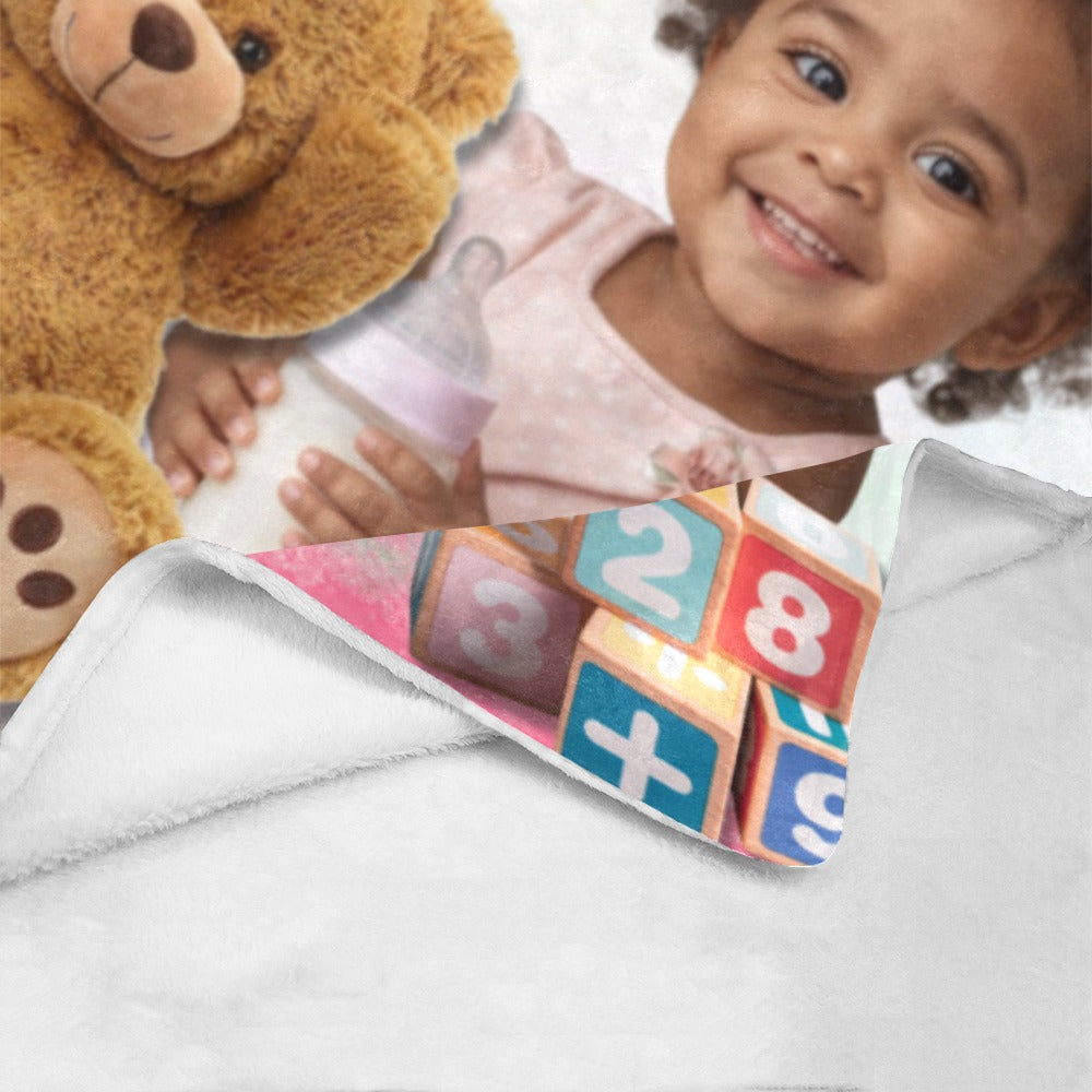 Child holding a teddy bear and baby bottle with educational blocks on a blanket